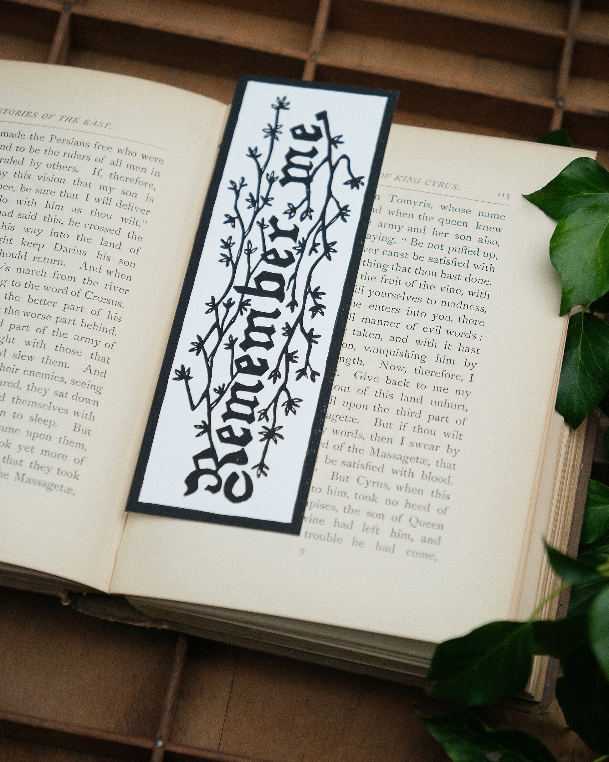 Open book with a decorative bookmark featuring the text 'Remember me' on a wooden surface.