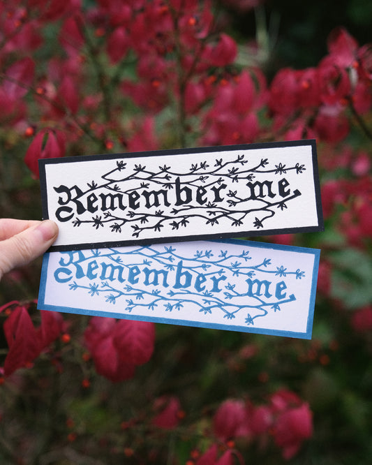 Two 'Remember me' bookmarks held against a blurred red leafy background
