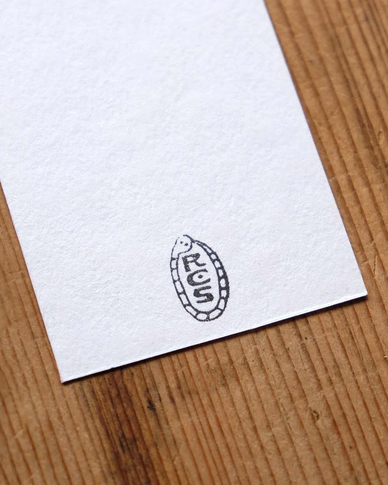 White paper with a black artist's stamp in the shape of a snake, on a wooden surface