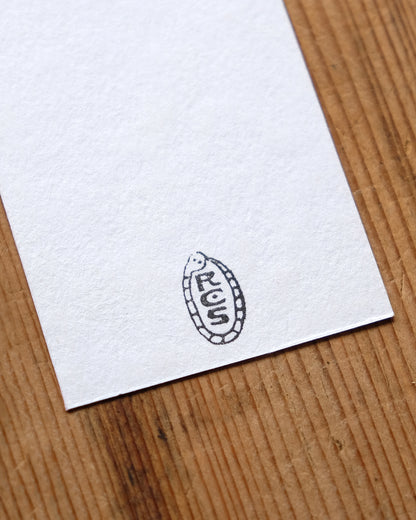 White paper with a black artist's stamp in the shape of a snake, on a wooden surface