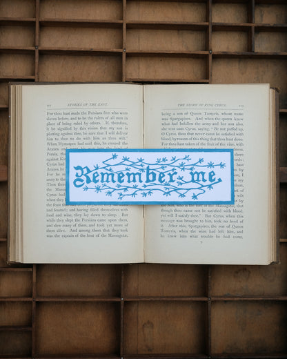 Open book with a blue 'Remember me' bookmark on a wooden background